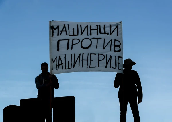 Силуете двоје студената са транспарентом Машинци против машинерије на фону плавог неба